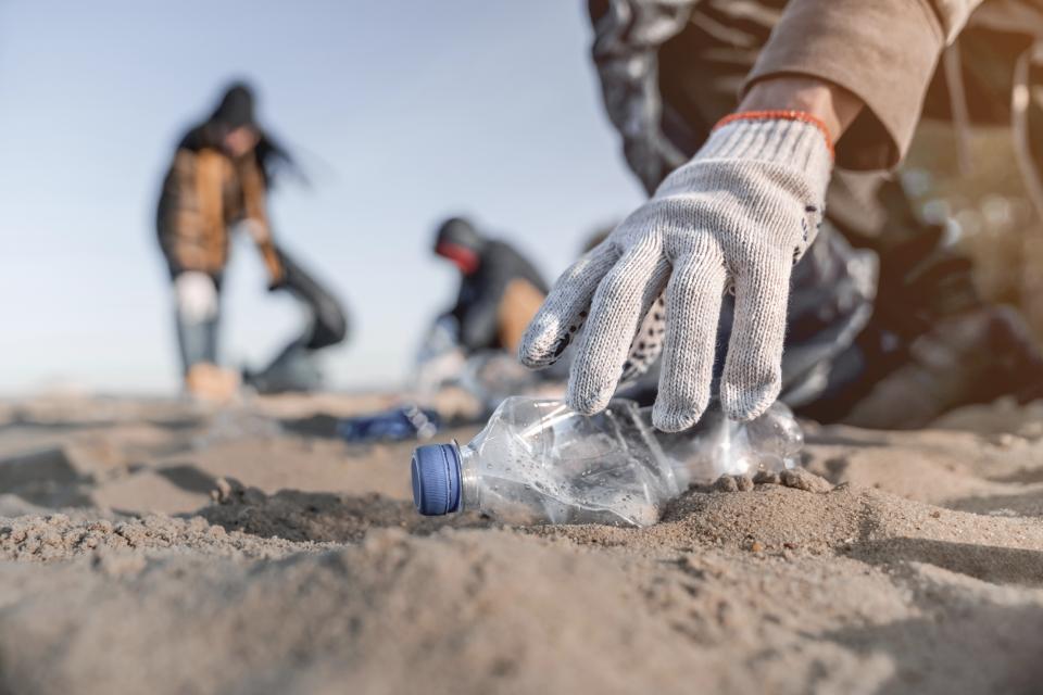 Person med handsker på samler en brugt plastflaske op fra strand